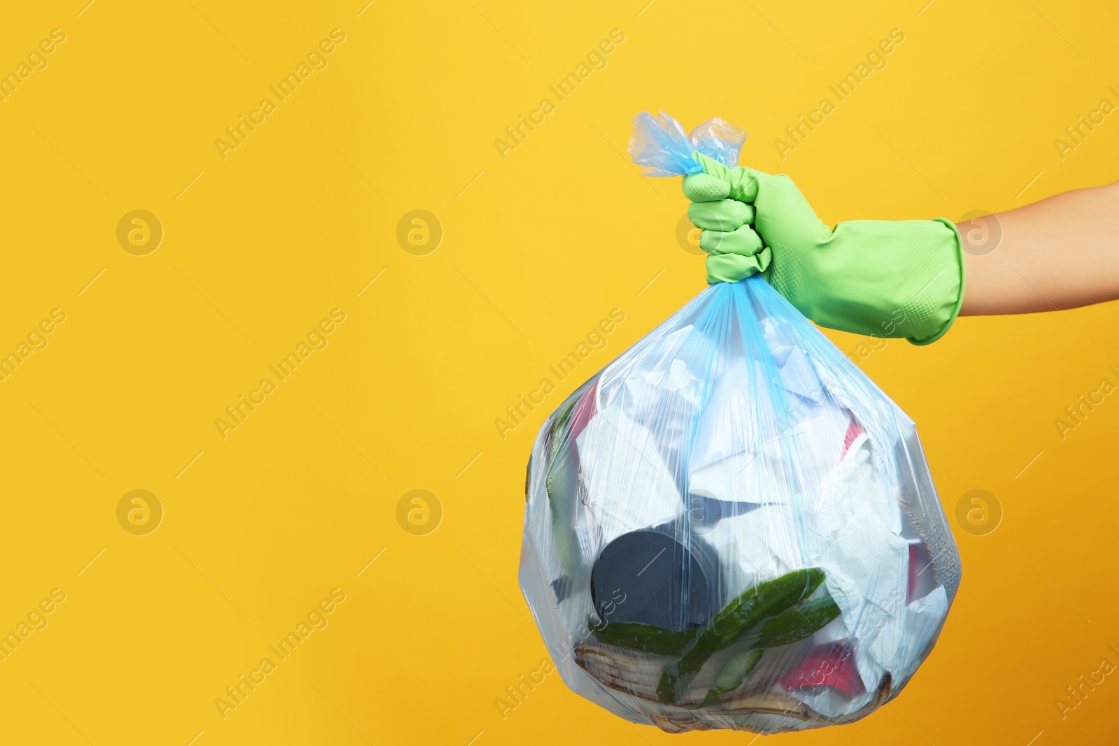 Photo of Woman holding full garbage bag on yellow background, closeup. Space for text