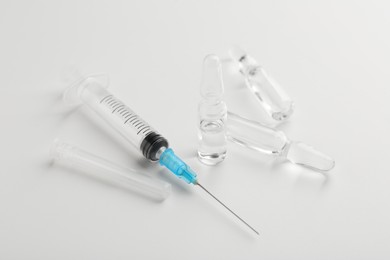 Photo of Glass ampoules with liquid and syringe on white background, closeup