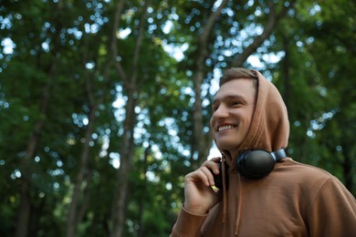 Photo of Smiling man with headphones walking in park. Space for text