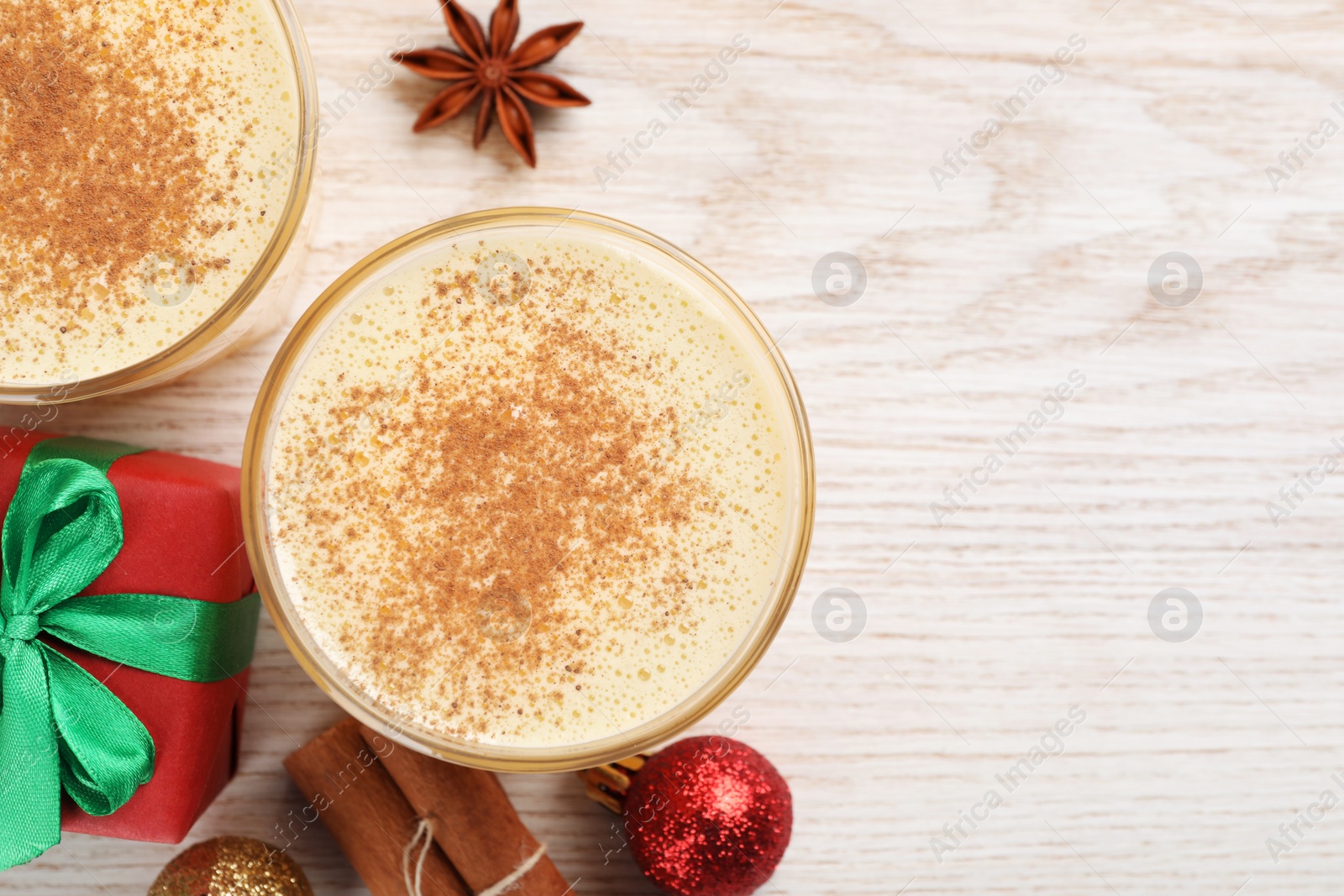 Photo of Tasty eggnog with cinnamon, anise star and Christmas decorations on white wooden table, flat lay. Space for text