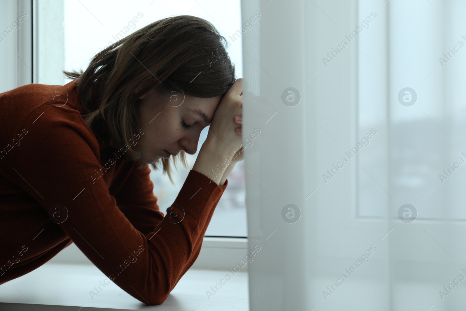 Photo of Sad young woman near window indoors, space for text