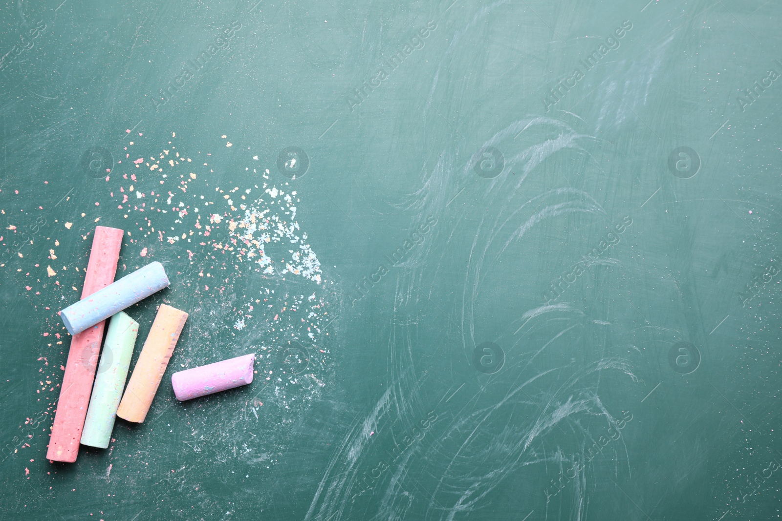 Photo of Pieces of color chalk on greenboard, flat lay. Space for text