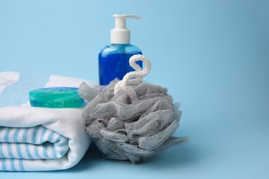 Photo of Grey shower puff, cosmetic products and towel on light blue background, space for text