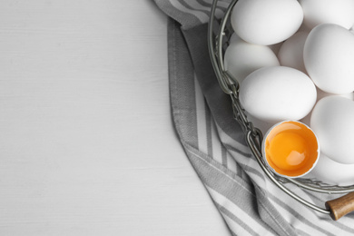 Photo of Many raw chicken eggs in metal basket on white wooden table, flat lay. Space for text