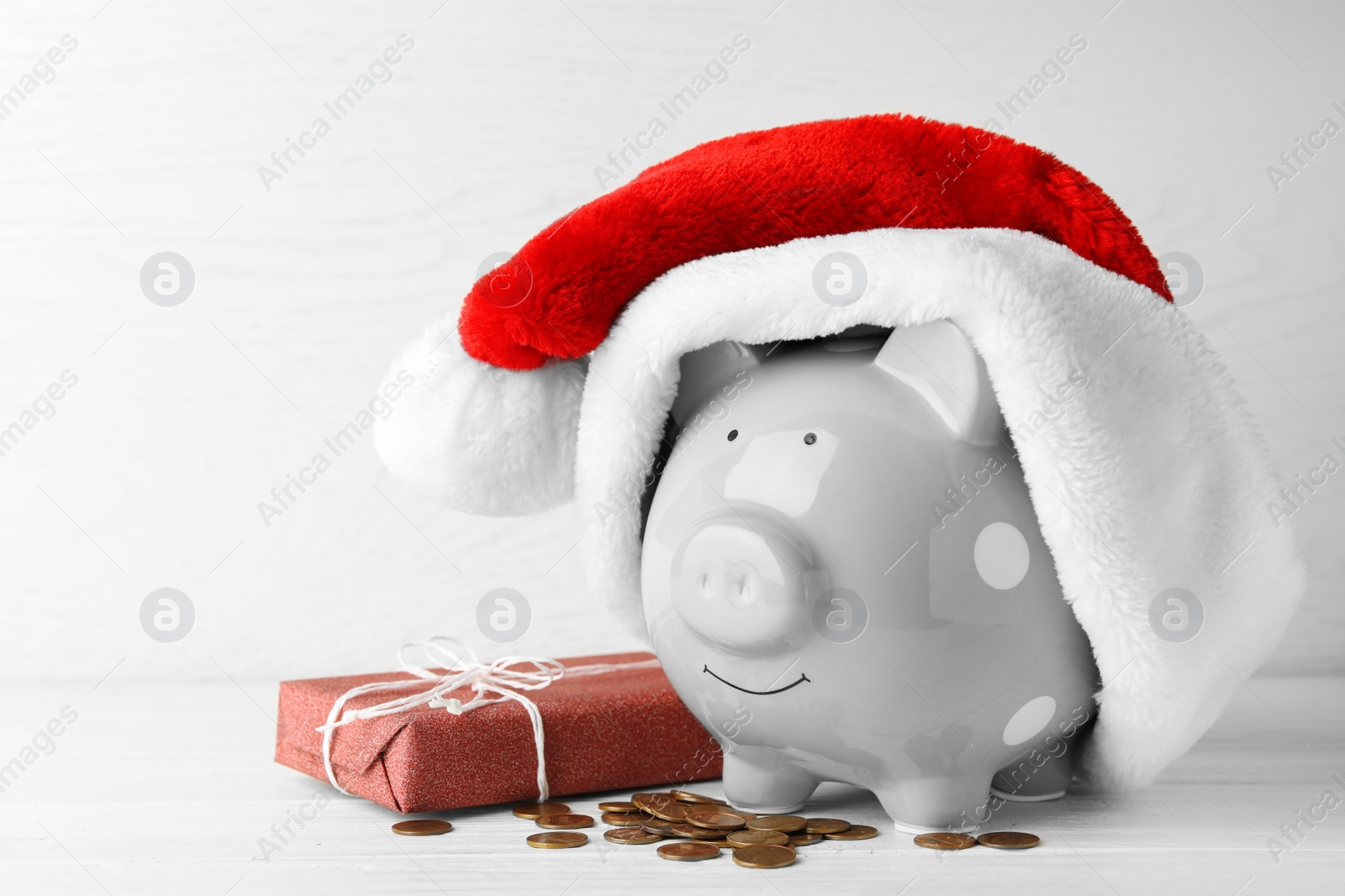 Photo of Piggy bank with Santa hat, gift box and coins on white wooden table