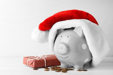 Photo of Piggy bank with Santa hat, gift box and coins on white wooden table