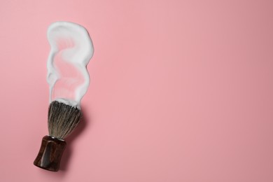 Photo of Brush with shaving foam on pink background, top view. Space for text