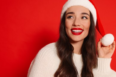 Photo of Christmas celebration. Beautiful young woman in Santa hat on red background, space for text