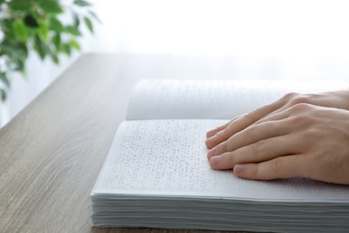 Blind man reading book written in Braille at table, closeup