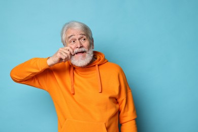 Photo of Senior man touching mustache on light blue background, space for text