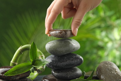 Photo of Woman stacking stones against blurred background, closeup. Zen concept