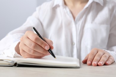 Photo of Woman writing in notebook at wooden table in office, closeup