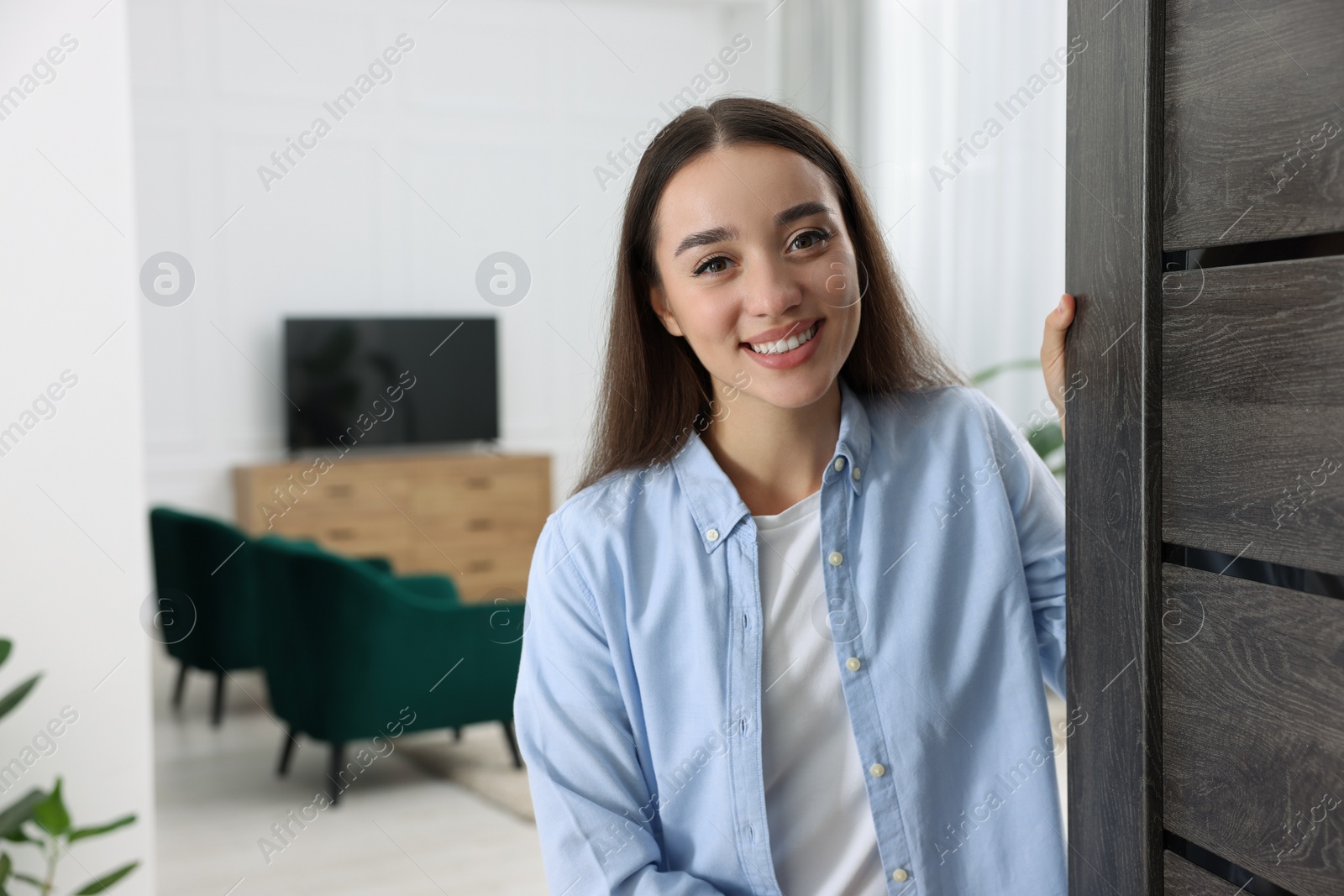 Photo of Happy woman standing near door, space for text. Invitation to come indoors