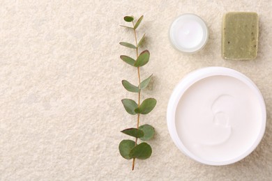 Photo of Body care cream in open jars, eucalyptus branch and soap bar on light textured table, flat lay. Space for text