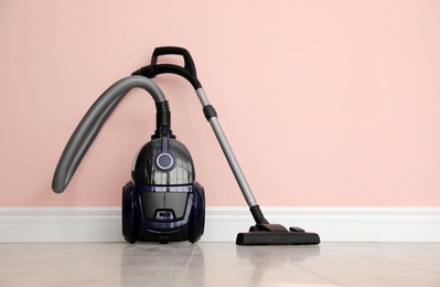 Photo of Modern vacuum cleaner near pink wall indoors