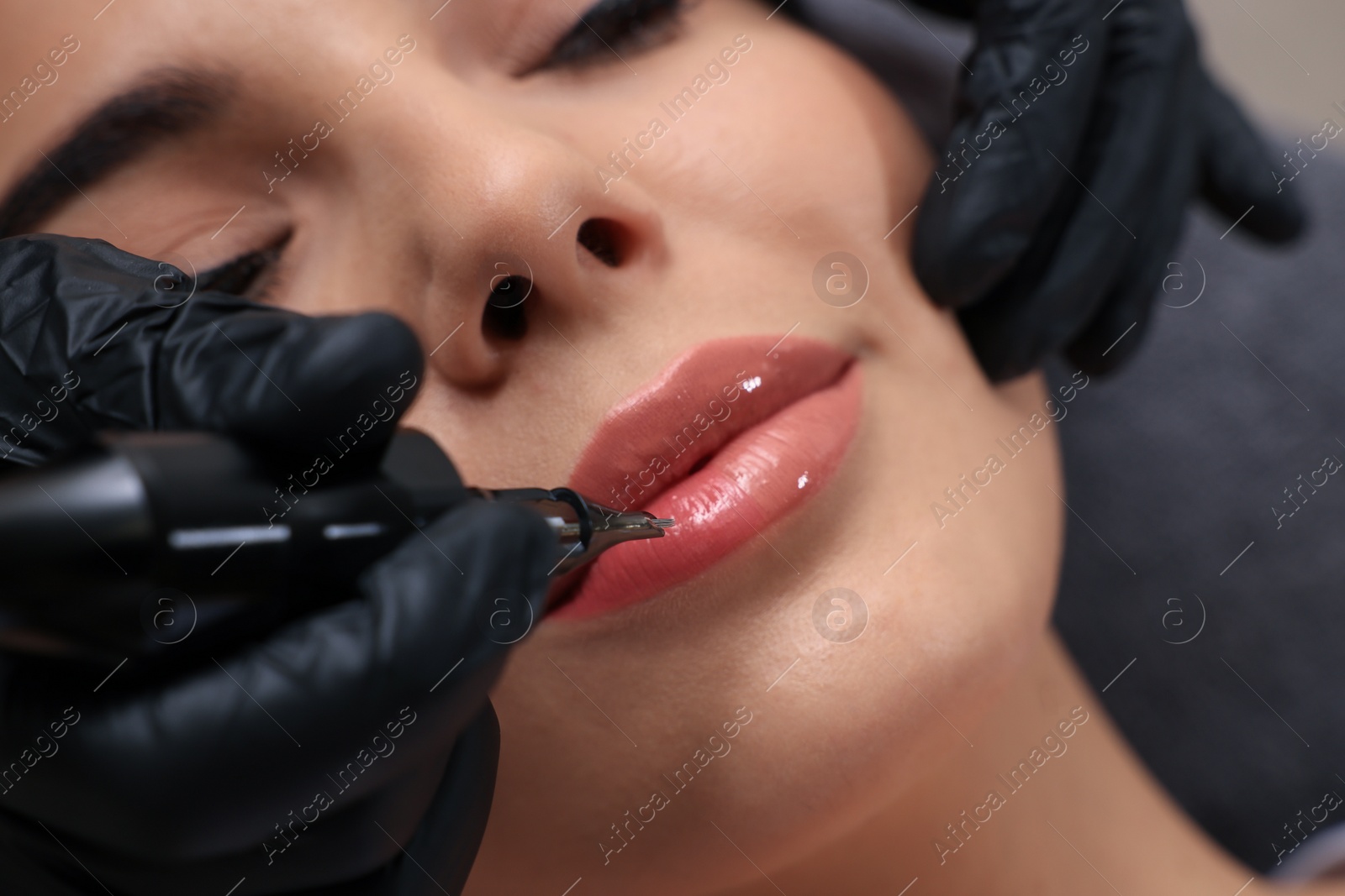 Photo of Young woman undergoing procedure of permanent lip makeup in tattoo salon, closeup