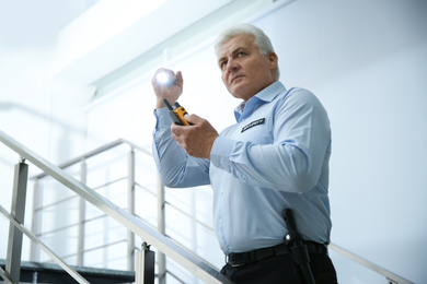 Photo of Professional security guard with portable radio set and flashlight on stairs indoors