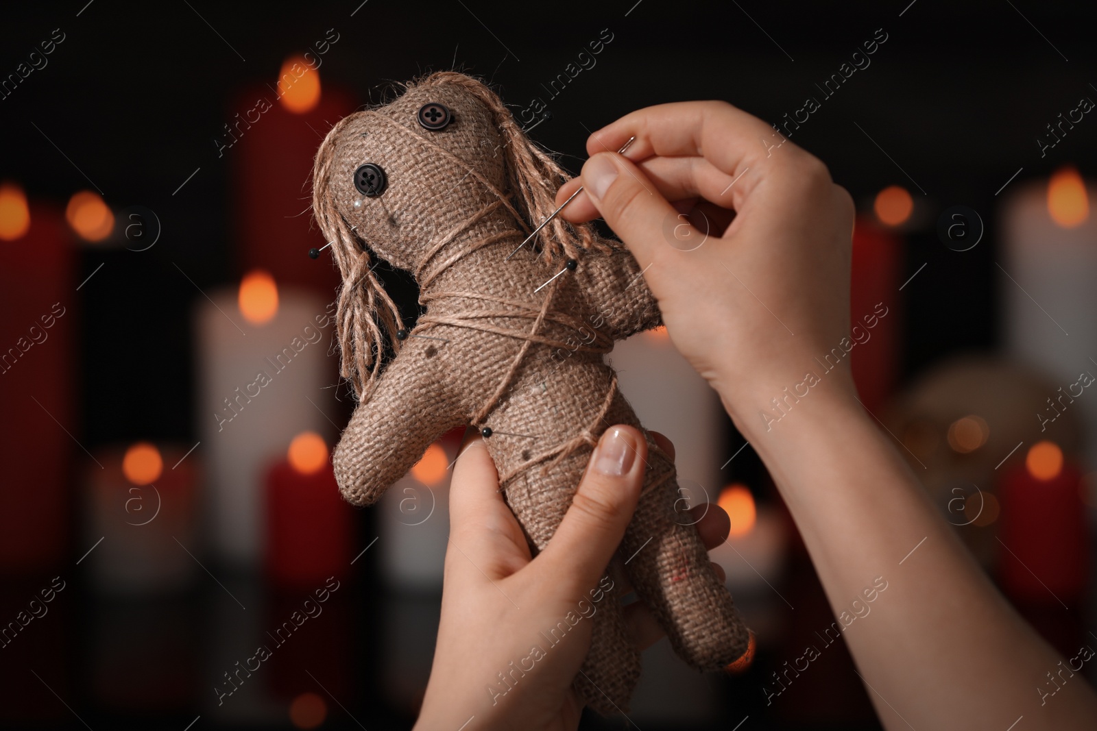 Photo of Woman stabbing voodoo doll with pin in dark room, closeup. Curse ceremony