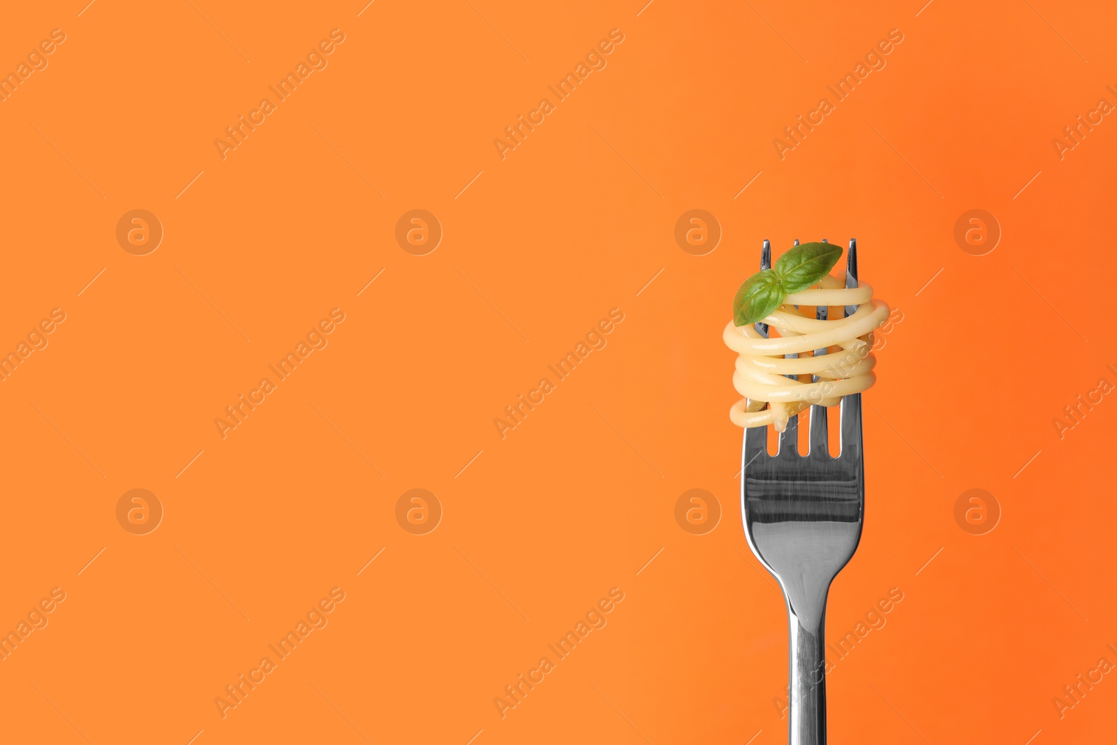 Photo of Fork with tasty pasta and basil on orange background, space for text