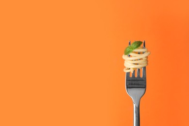 Fork with tasty pasta and basil on orange background, space for text