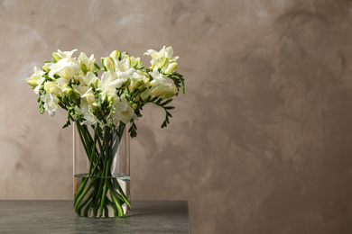 Photo of Beautiful freesia flowers in vase on grey table. Space for text