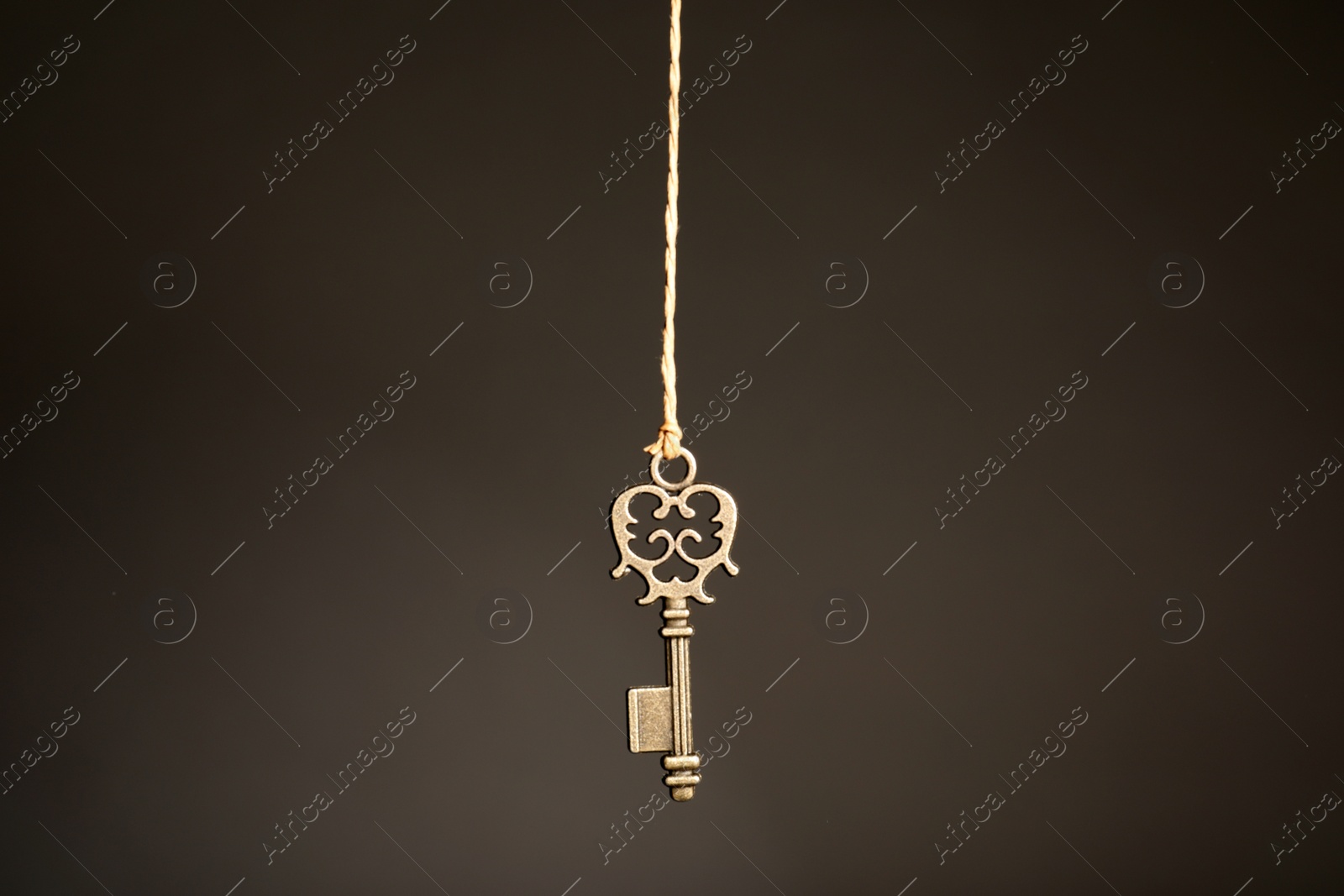 Photo of Bronze vintage ornate key hanging on thread against dark background