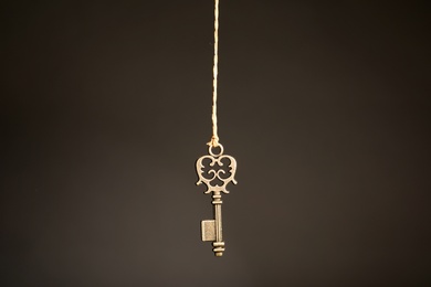 Photo of Bronze vintage ornate key hanging on thread against dark background