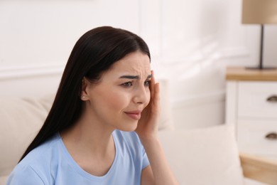 Photo of Young woman suffering from migraine at home, space for text