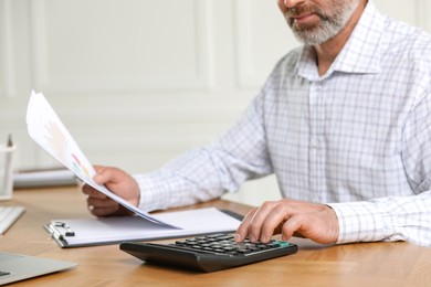 Photo of Professional accountant using calculator at wooden desk indoors, closeup