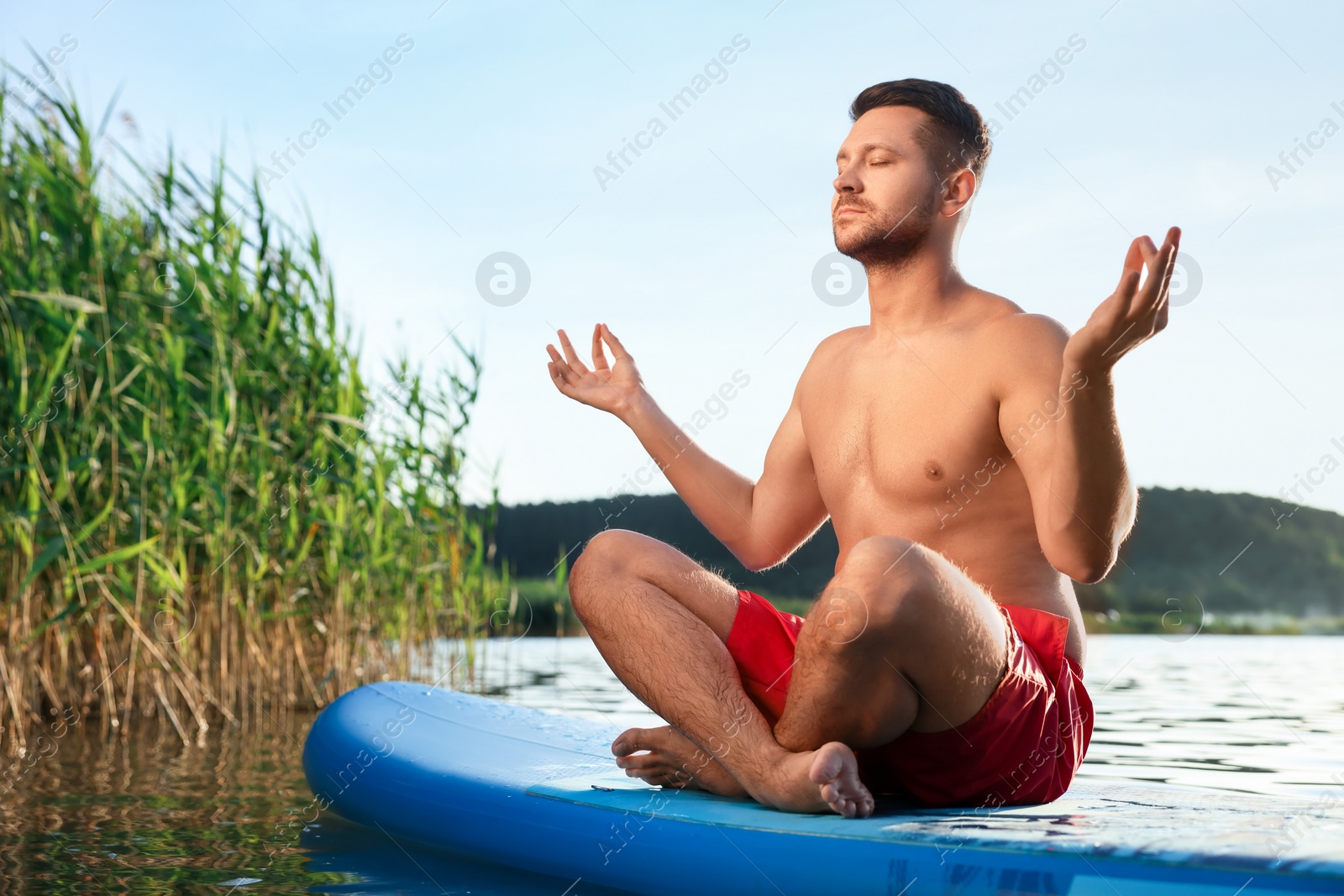 Photo of Man meditating on light blue SUP board on river at sunset