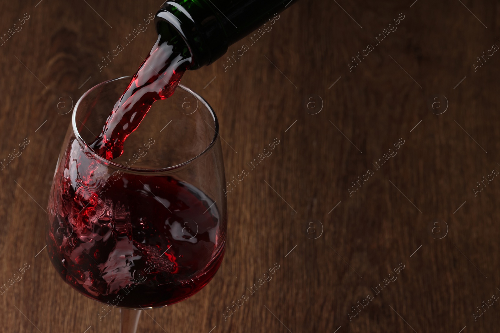 Photo of Pouring tasty red wine in glass at wooden table, closeup. Space for text