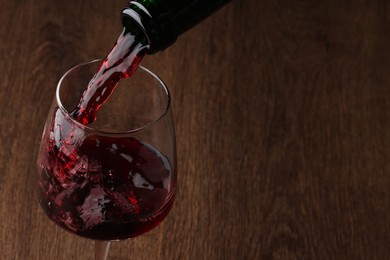 Photo of Pouring tasty red wine in glass at wooden table, closeup. Space for text