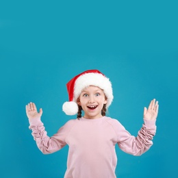 Image of Excited little child in Santa hat on light blue background. Christmas celebration