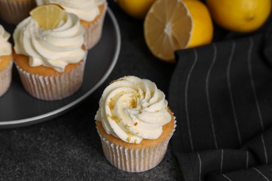 Delicious cupcakes with white cream, lemon zest and lemons on grey table, closeup