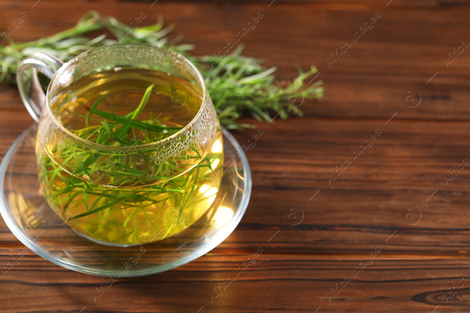 Photo of Cup of homemade tarragon tea on wooden table. Space for text