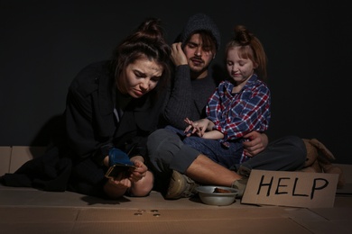 Photo of Poor family with HELP sign and coins on floor near dark wall