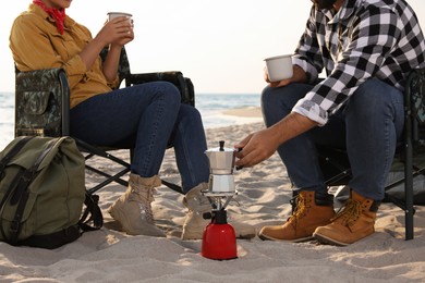 Photo of Couple resting in camping chairs on beach, closeup. Making coffee