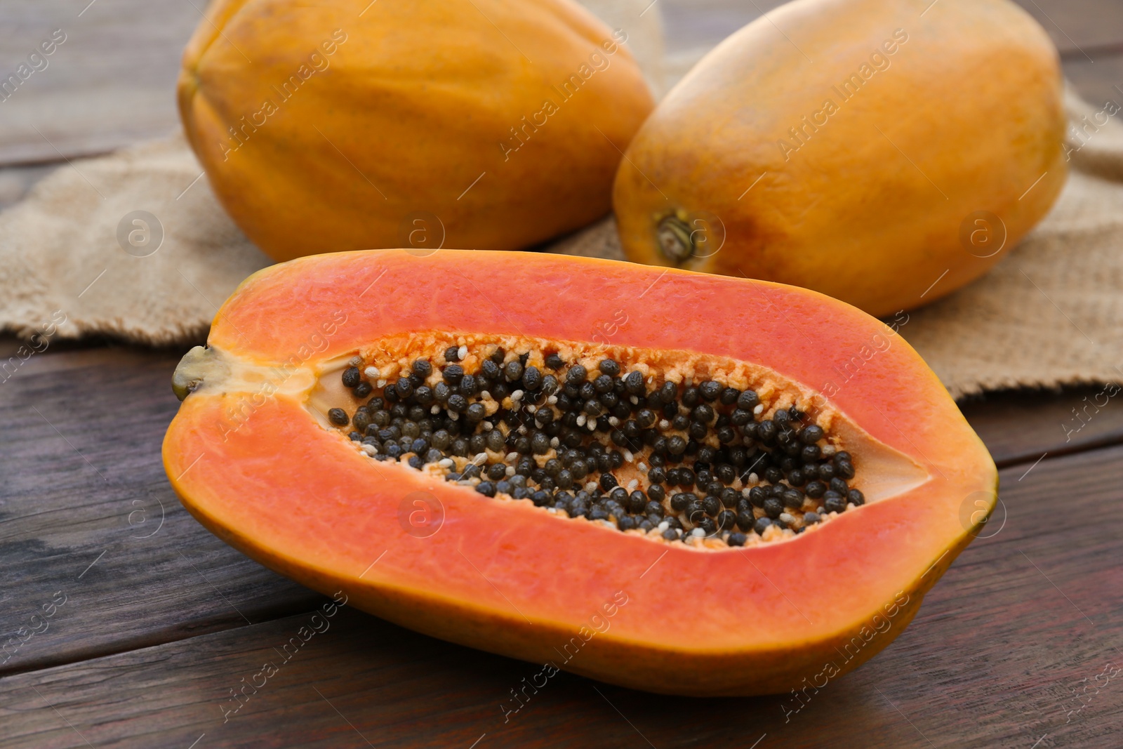 Photo of Tasty cut and whole papaya fruits on wooden table, closeup