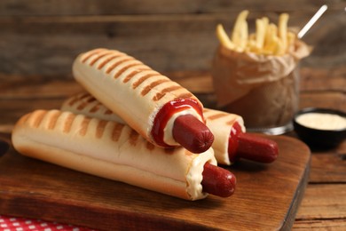 Photo of Delicious french hot dogs, fries and dip sauce on wooden table, closeup