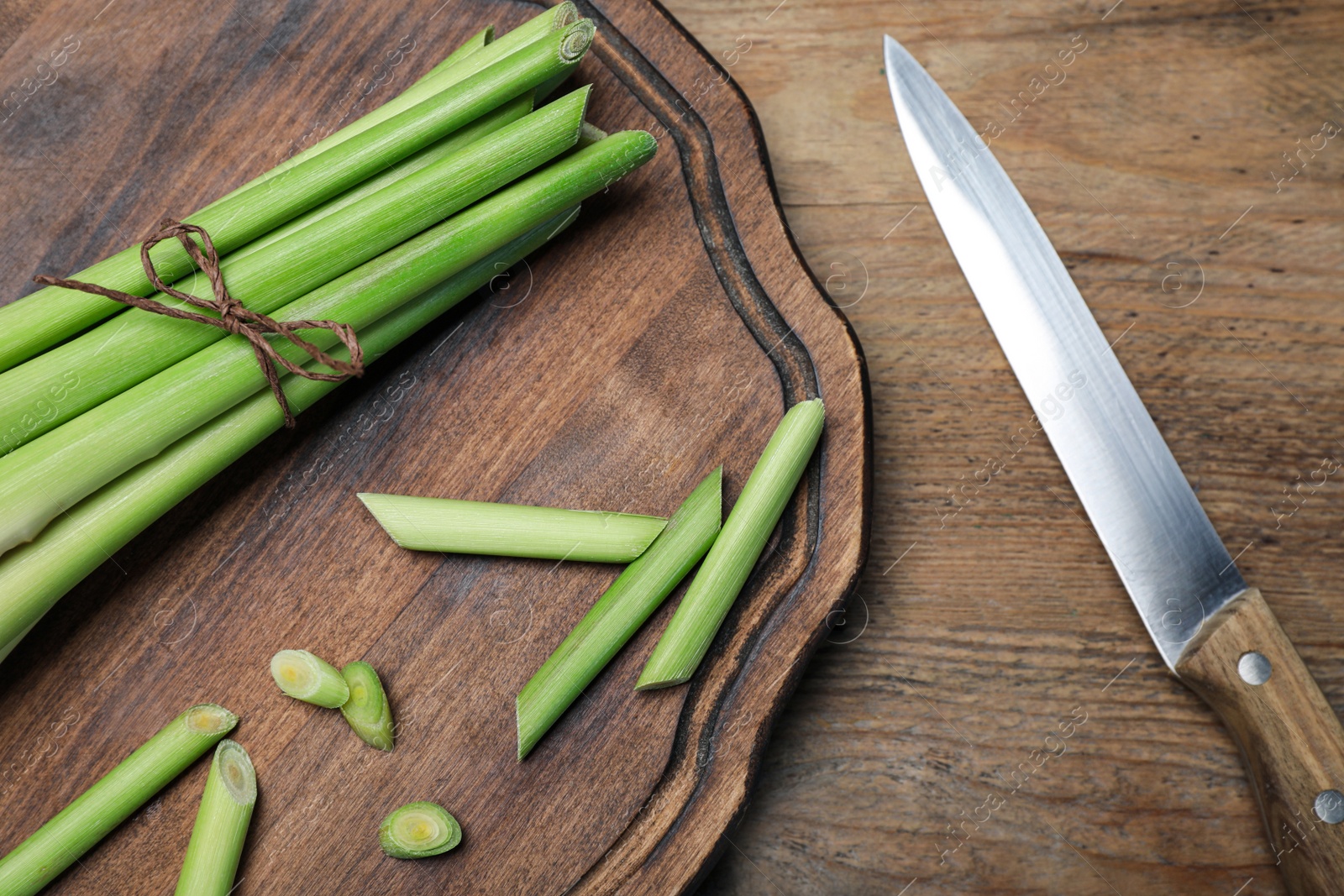 Photo of Fresh lemongrass, knife and cutting board on wooden table, flat lay