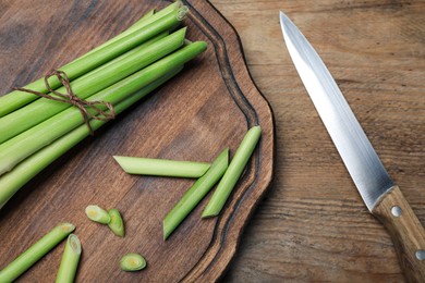 Fresh lemongrass, knife and cutting board on wooden table, flat lay