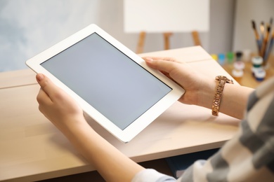 Woman using modern tablet at workplace indoors, closeup. Space for design