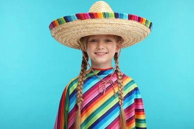 Photo of Cute girl in Mexican sombrero hat and poncho on light blue background