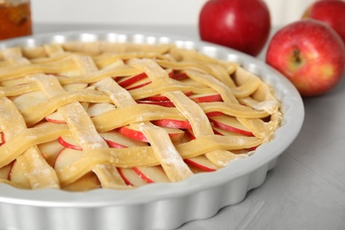 Photo of Raw traditional English apple pie in baking dish on light grey table, closeup