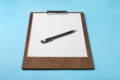 Photo of New wooden clipboard with sheet of blank paper and pen on light blue background