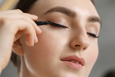 Makeup product. Woman applying black eyeliner on blurred background, closeup