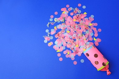 Photo of Colorful confetti and streamers bursting out of party cracker on blue background, flat lay. Space for text