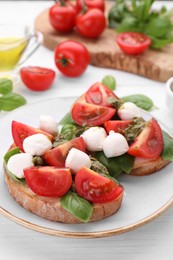 Photo of Delicious Caprese sandwiches with mozzarella, tomatoes, basil and pesto sauce on white wooden table, closeup