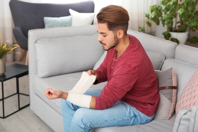 Young man applying bandage on injured arm at home. First aid