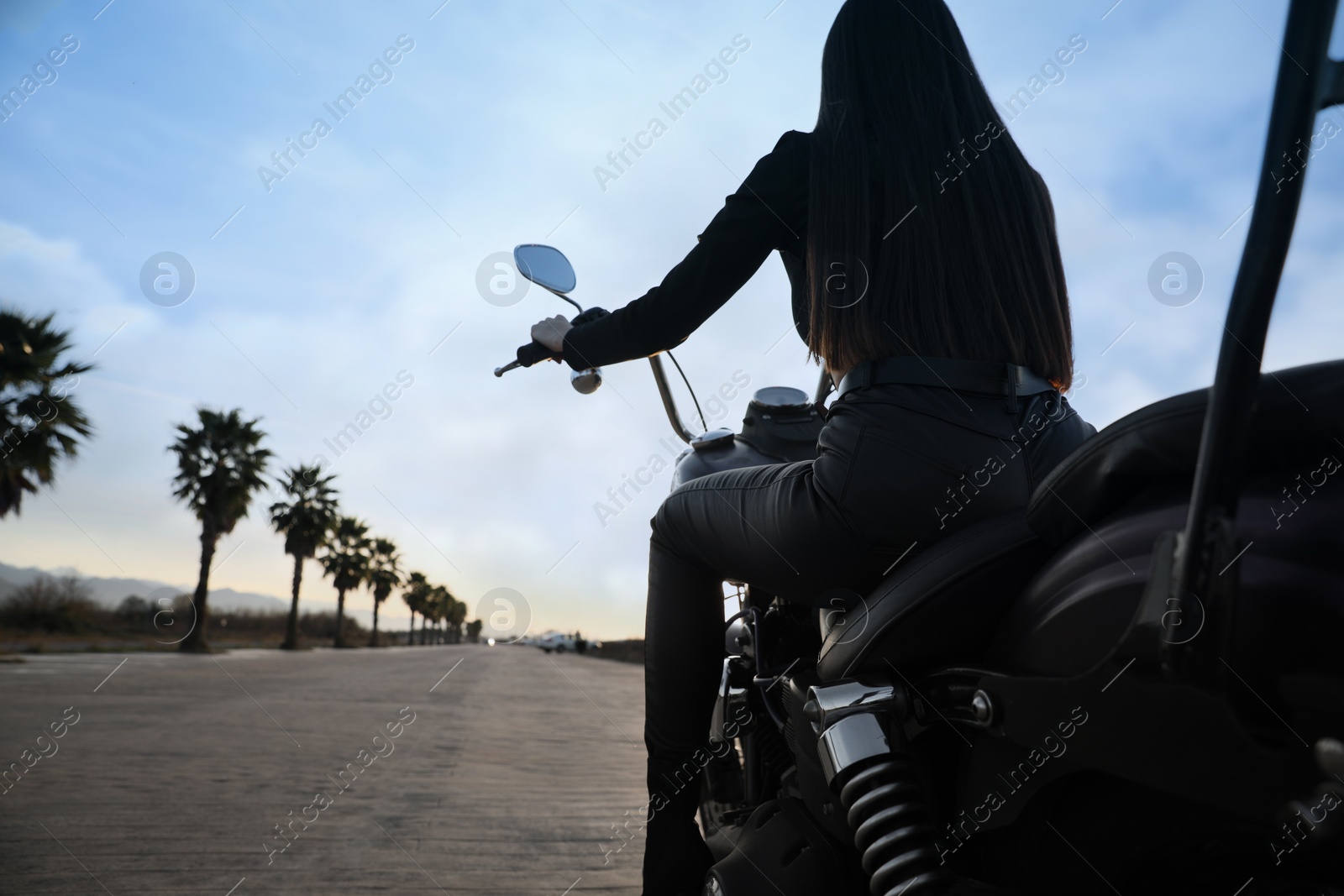 Photo of Woman riding motorcycle at sunset, back view. Space for text